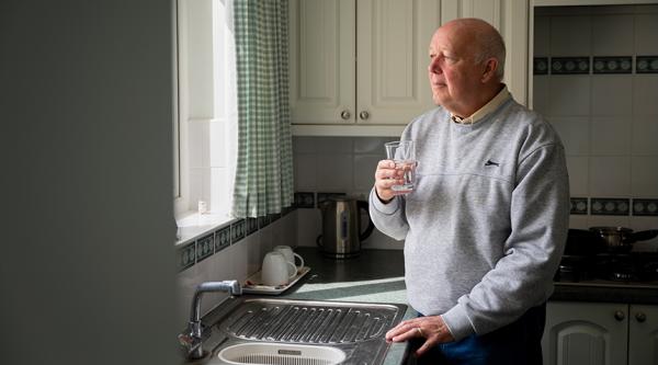 Man stood by kitchen sink, holding a glass of water and staring out of the window